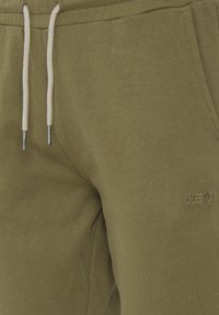 Olivgrüne Jogginghose mit strukturiertem Finish, ausgestattet mit einem Kordelzug mit Metallenden und einem gestickten "BLEND"-Logo an der Seite.