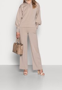 Beige zip-up sweatshirt med vida ärmar, matchat med vida byxor. Tillbehör inkluderar en beige handväska och ljusa klackar.