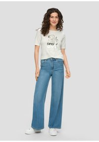 Witte cropped t-shirt met zilveren pailletten opdruk met de tekst "GRATITUDE", gecombineerd met lichtblauwe wijde jeans en witte sneakers.