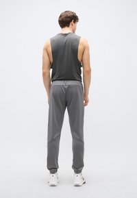 Pelēkas sporta bikses ar sānu paneļiem, elastīgu jostu un sašaurinātām aprocēm, kopā ar pelēku bezroku topu, skatāms no aizmugures.