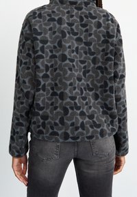 Fleece jacket in dark gray with a textured pattern of black and lighter gray abstract shapes. Features a collar and long sleeves.
