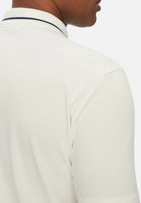 Polo de color blanco roto con un tejido texturizado. Presenta un cuello clásico con un ribete azul marino. Manga corta y un diseño ajustado.