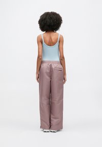 Hellblaues, geripptes Tanktop mit dünnen Trägern, kombiniert mit lockeren, rosa, wasserabweisenden Hosen mit elastischem Bund und Seitentasche.