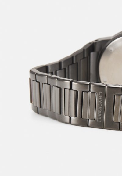 Metal watch with a dark gray bracelet featuring elongated rectangular links. Brand name "FERRAGAMO" engraved on one link. Round silver face.