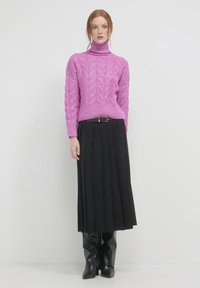 Rosa Kabelstrick-Turtleneck-Pullover kombiniert mit einem schwarzen Faltenrock und knielangen schwarzen Stiefeln. Das Outfit zeichnet sich durch kontrastierende Texturen aus.