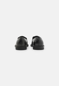 Mocasini negri din piele, cu o textura netedă, vârf rotunjit și design minimalist. Prezintă un logo embosat pe toc și talpă din cauciuc plat.
