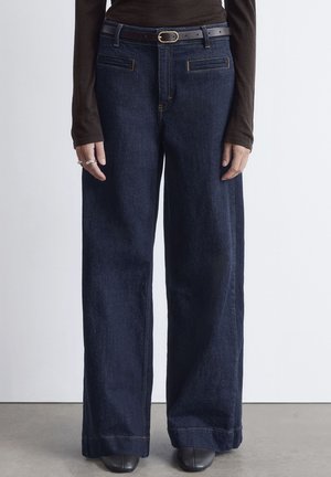 Dark denim wide-leg jeans with front pockets, subtle orange stitching, and a black belt. Smooth texture and structured shape.