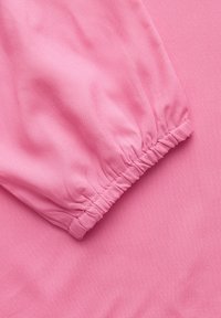 Tissu rose à texture lisse, avec un poignet froncé à la fin de la manche, mettant en valeur son élasticité et son tombé doux.