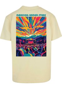 Camiseta de manga corta en color beige que presenta una colorida escena de concierto con siluetas de un público, montañas y un vibrante fondo de atardecer.