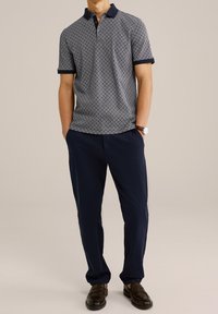 Polo tričko s krátkým rukávem v námořnickém vzoru, kontrastní límec; spárováno s námořnickými kalhotami a tmavými mokasíny. Neformální outfit.