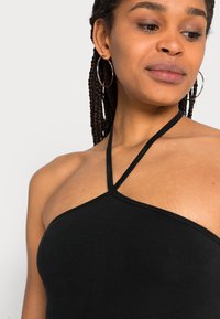 Top halter preto feito de um tecido macio e texturado. Apresenta alças finas que formam um formato em V na gola, com uma silhueta ajustada.