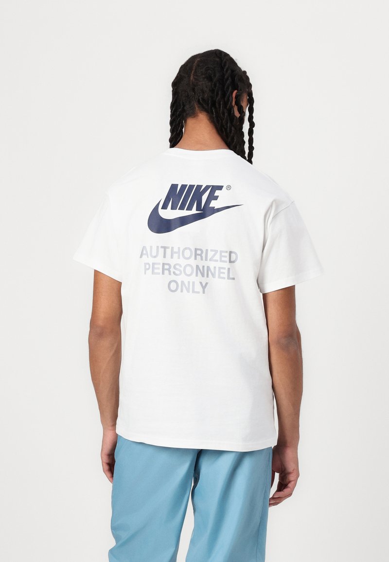 Balta trumpomis rankovėmis marškinėliai su dideliu tamsiai mėlynu Nike logotipu ir pilku užrašu "LEIDŽIAMI TIK ĮGULOS NARIAI" ant nugaros. Minkšta medvilnės medžiaga.