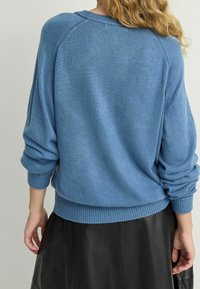 Niebieski sweter dzianinowy o luźnym kroju, teksturowany materiał, prążkowane mankiety i dół, oraz opadające ramiona, w zestawieniu z czarną skórzaną spódnicą.