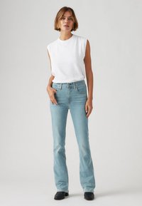 Svetlo modri široki jeans z visokim pasom, v kombinaciji z belim topom brez rokavov. Jeans imajo klasično denim teksturo in rahel bledik.