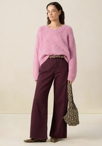 Pull en V rose en tricot, pantalon large bordeaux, ceinture à imprimé animal, sac à main assorti et chaussures texturées avec un motif serpent.