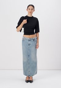 Zwart cropped top, hooggevoerde lichtblauwe denim maxi rok, zachte textuur, getailleerd design, gecombineerd met zwarte puntig hakken en een kleine witte tas.