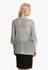 Silver, öppen stickad cardigan med diamantmönster och trekvartslånga ärmar, i kombination med en tight svart kjol.