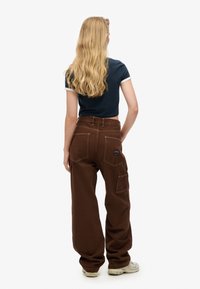 Pantalones anchos marrones con bolsillos laterales, con una tela texturizada y costuras en contraste, combinados con una blusa corta de manga azul marino.