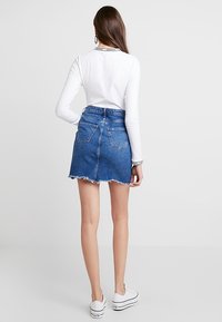 Džínová sukně s třepeným lemem, čtyřmi kapsami a vysokým pasem, spárovaná s dlouhým bílým topem s potiskem na výstřihu.