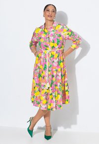 Vestito colorato rosa con motivi floreali e limone; presenta una chiusura frontale con bottoni, maniche a tre quarti, gonna a strati e una cintura in vita.