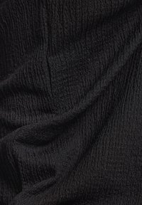 Schwarzer strukturierter Stoff mit sichtbaren kleinen Rillen, weichen Falten und einer leicht glänzenden Oberfläche.