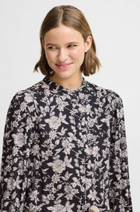 Blusa nera floreale con design button-up, maniche lunghe e colletto, con motivi floreali bianchi e una texture di tessuto liscia.