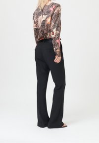 Blouse à manches longues à motif floral avec un pantalon noir. La blouse présente une palette de couleurs mélangées avec des accents de rose, crème et noir.