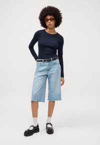 Tengerész hosszú ujjú felső, világoskék farmer culottes nyers szegéllyel, fekete stúdiózott öv, és tömör fekete platform cipők fehér zoknival.