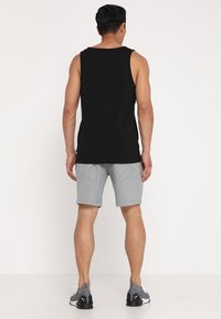 Musta puuvillainen hihaton toppi yhdistettynä harmaisiin shortseihin; molemmissa rento istuvuus. Jalkineissa musta-harmaa malli ja teksturoitu kangas.