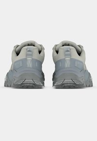 Ζευγάρι γκρι και ανοιχτού μπεζ παπούτσια πεζοπορίας, ορατά από πίσω, με υφασμένα πέλματα και θηλιές στο πίσω μέρος στον αστράγαλο.