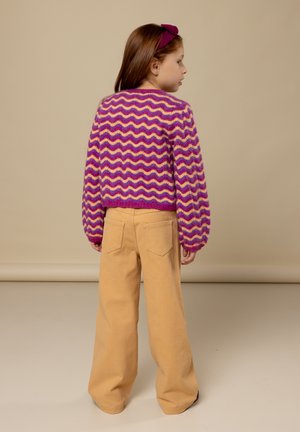 Gebreide trui met een roze en paars zigzagpatroon, gecombineerd met beige wijde broekspijpen. De trui heeft lange mouwen en een cropped pasvorm.