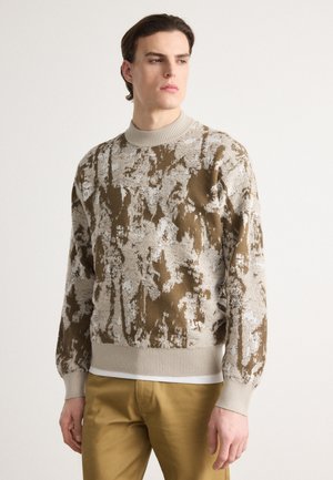 Beige and brown patterned sweater with a crew neckline and ribbed cuffs, made of textured knit material. Worn with khaki pants.
