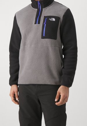 Szary i czarny polarowy pulower z wysokim kołnierzem, zamkiem do połowy długości, kieszenią na piersi oraz niebieskimi akcentami na zamku. Materiał o fakturowanej powierzchni.