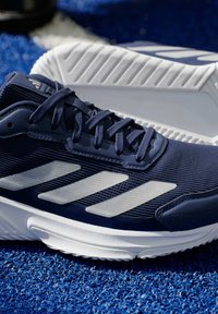 Morska tenisówka sportowa z teksturowanej tkaniny, białymi paskami i gumową podeszwą. Charakteryzuje się smukłym designem i solidnym systemem sznurowania.