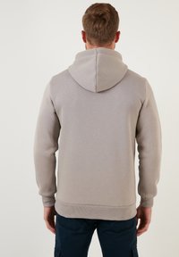 Sudadera gris claro de corte relajado, con capucha, puños acanalados y una textura en la tela. Sin logotipos ni patrones visibles.