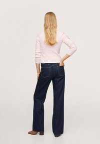 Helles rosa, geripptes Strickpullover kombiniert mit dunkelblauen weit geschnittenen Jeans, die über zwei hintere Taschen und einen sichtbaren Bund verfügen. Braune Absatzschuhe.