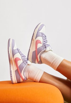 Sneakers Nike Dunk charakteryzują się fioletowo-białym wzorem z różowym swoosh, teksturowaną gumową podeszwą i są zestawione z żebrowanymi białymi skarpetkami.