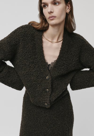 Texturert, mørkebrun cardigan med dyp V-hals, frontknapper og senkede skuldre, kombinert med en undertrøye med blonder.