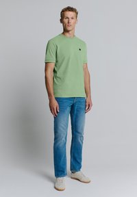 Groene katoenen t-shirt met korte mouwen en een ronde halslijn. Draag het met lichtblauwe jeans en witte sneakers. Minimalistisch zwart logo detail.