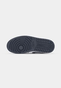 Semelle d'une chaussure de sport noire Nike avec un motif de crampons circulaires et le logo Nike sur un fond clair uni.