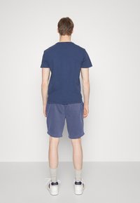 Tmavě modré bavlněné tričko spárované se světle modrými šortkami. Šortky mají ohrnutý lem a zadní kapsu. Bílé tenisky se šedými ponožkami.