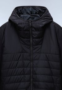 Černá péřová bunda se zipem vpředu, izolovaným prošívaným tělem a kapucí. Obsahuje kontrastní látku na ramenou a hladký povrch.