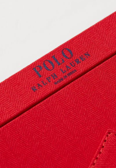 Sarkans audums ar zvīņveida rakstu, uz kura ir zils logo ar uzrakstu "POLO RALPH LAUREN" un frāzi "MADE IN INDIA".