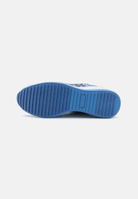 Modrá podrážka sneakers s textúrovaným gumovým detailom a drážkovanými vzormi; obsahuje značku "DKNY" vyrazenú na strednej podrážke.