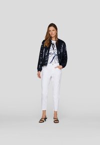 Navy sequined bomber jacket over a white graphic t-shirt, paired with white straight-leg trousers and black heeled sandals.