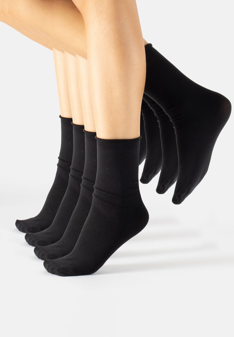 Cinque paia di gambe che indossano calze nere alla caviglia, disposte in fila con i piedi leggermente sollevati su uno sfondo bianco.