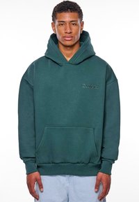 Grüne Kapuzenjacke mit einer Vordertasche, gerippten Bündchen und Saum. Mit gesticktem Text auf der Brust. Hergestellt aus weichem, strukturiertem Stoff.