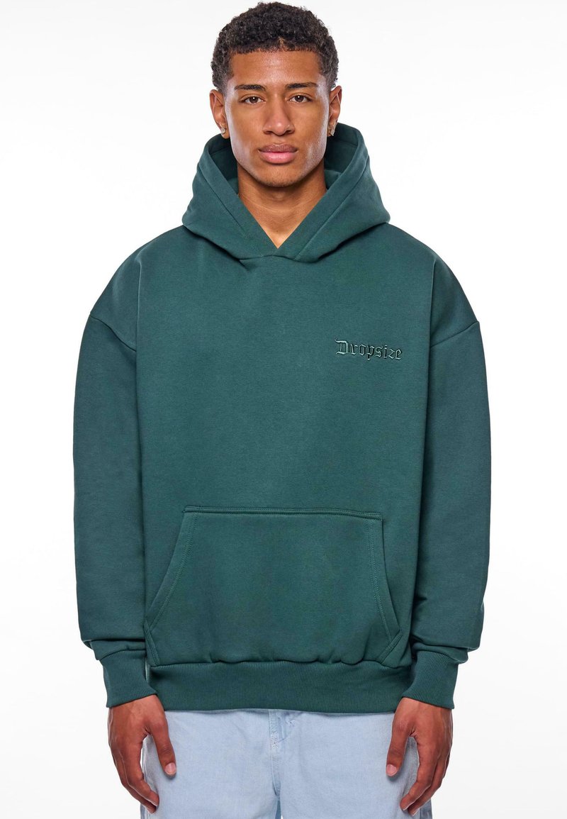Grüne Kapuzenjacke mit einer Vordertasche, gerippten Bündchen und Saum. Mit gesticktem Text auf der Brust. Hergestellt aus weichem, strukturiertem Stoff.