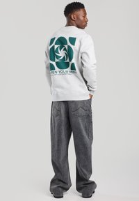 Light gray sweatshirt featuring a large green graphic with the text "OPEN YOUR MIND" on the back. Paired with gray, loose-fitting jeans.