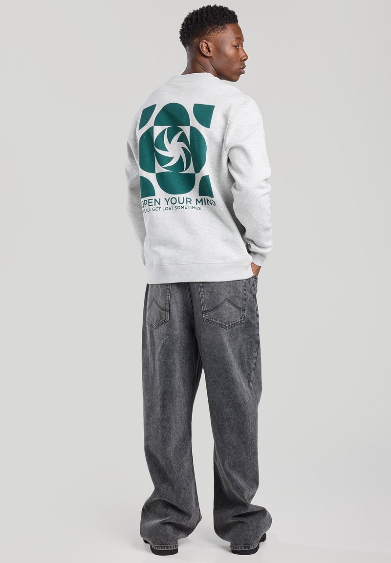 Light gray sweatshirt featuring a large green graphic with the text "OPEN YOUR MIND" on the back. Paired with gray, loose-fitting jeans.